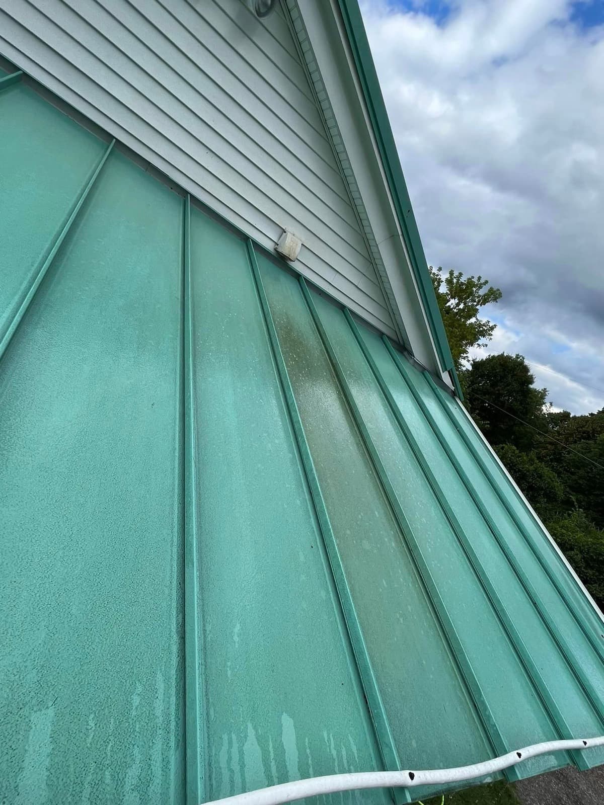 Green metal roof streaked with dirt before soft washing